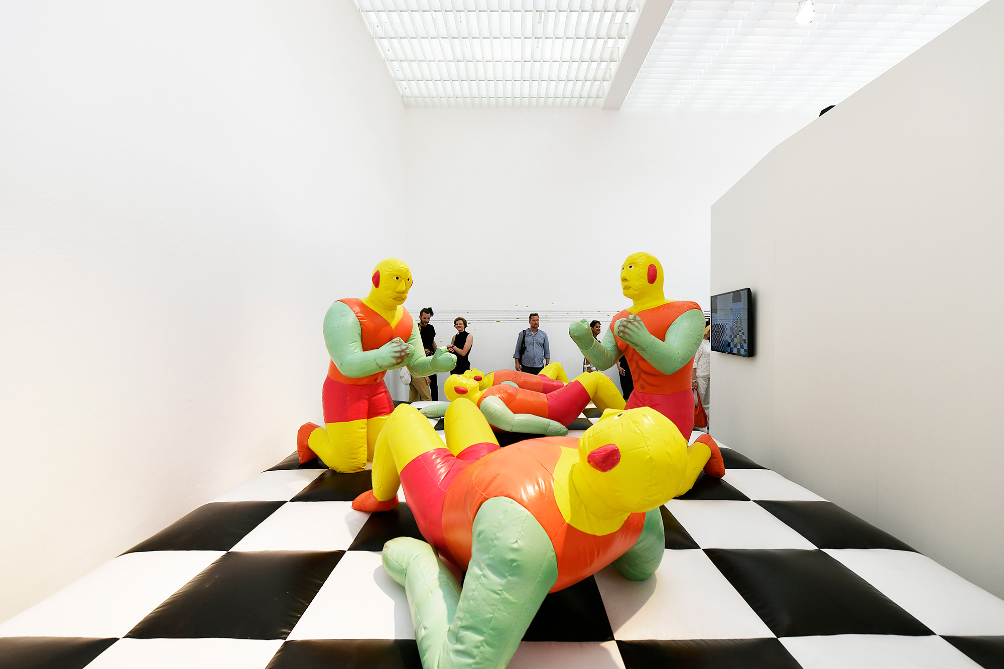 Colorful inflatable figures sit on knees and lay on backs on white-and-black checkerboarded-floor.