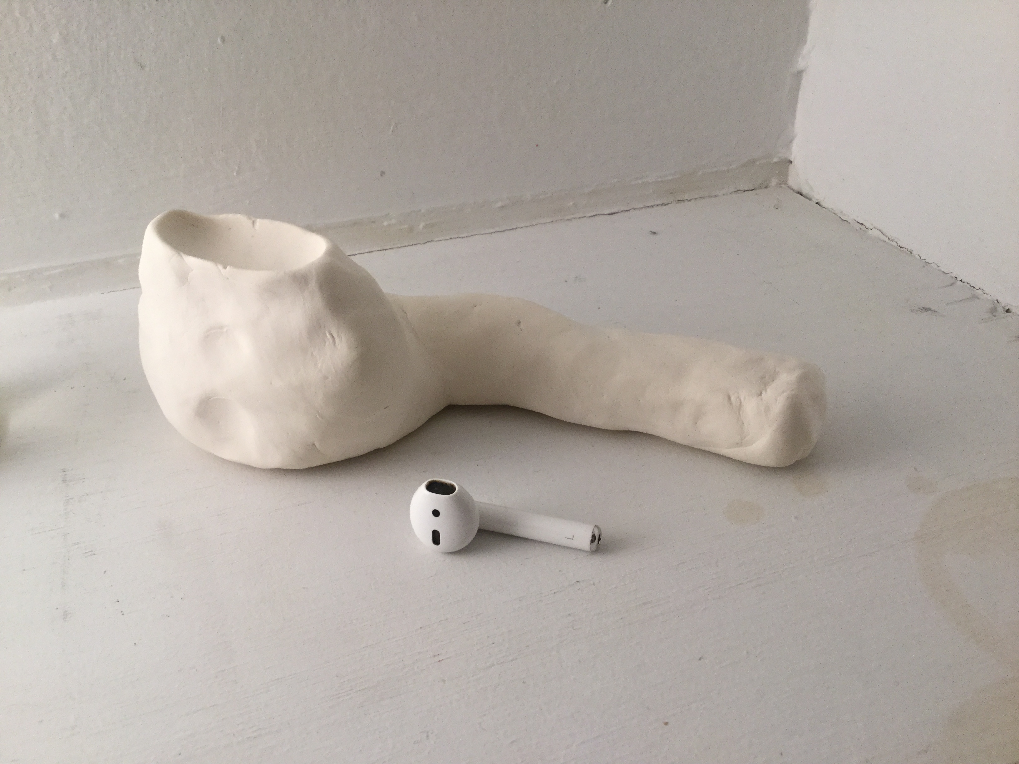 a larger white clay model of an Apple AirPod sits behind a smaller actual AirPod.